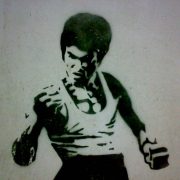 A black and white wall stencil of Bruce Lee in a fighting stance