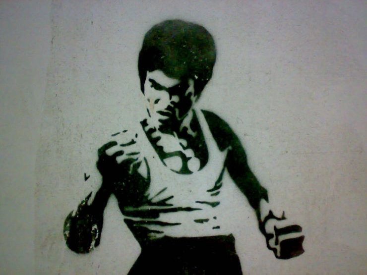 A black and white wall stencil of Bruce Lee in a fighting stance