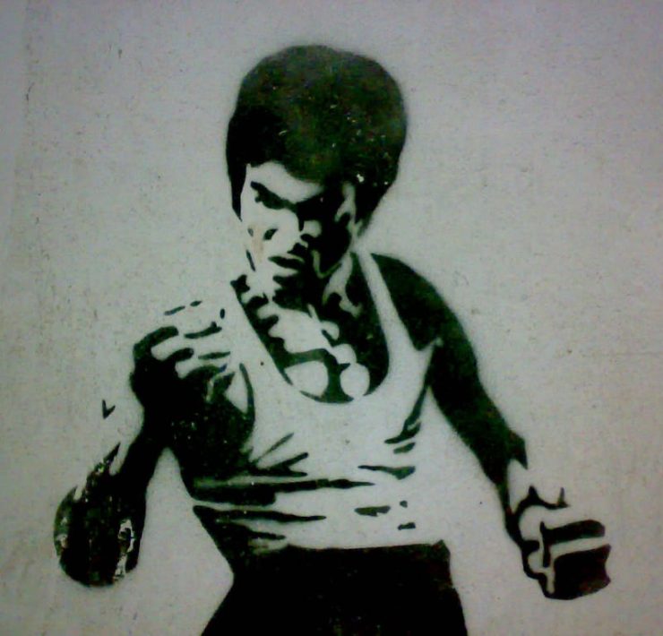 A black and white wall stencil of Bruce Lee in a fighting stance