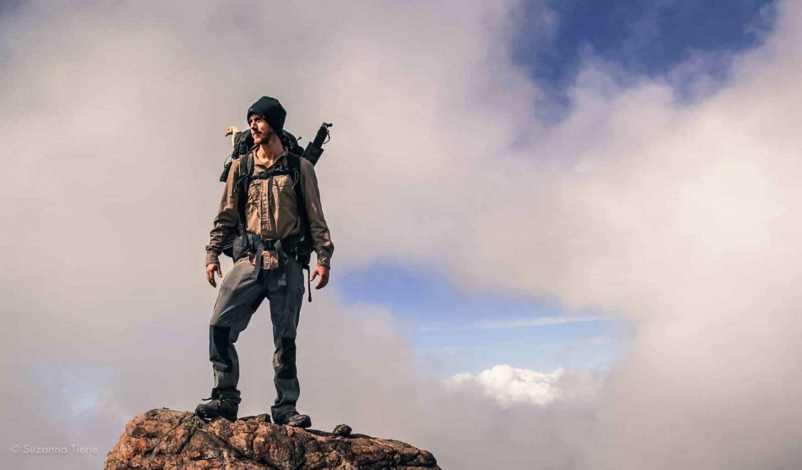 record breaking Adventurer Ash Dykes stands on top of a mountain in Madagascar. A chicken's head can be seen poking out of his rucksack. Pic taken by Suzanna Tierie