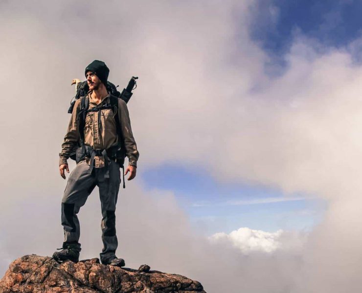 record breaking Adventurer Ash Dykes stands on top of a mountain in Madagascar. A chicken's head can be seen poking out of his rucksack. Pic taken by Suzanna Tierie
