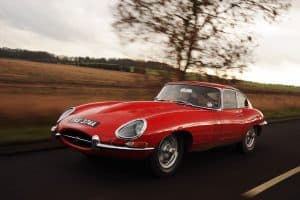 Red E Type Jaguar driving down a country road