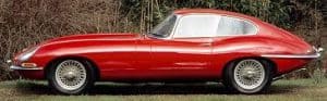 A red E Type Jaguar parked in front of some trees
