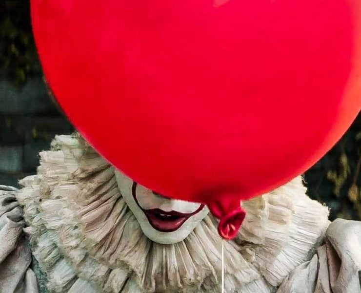 Picture of clown Pennywise from remake of IT. He is hiding behind red balloon so you can just see his mouth