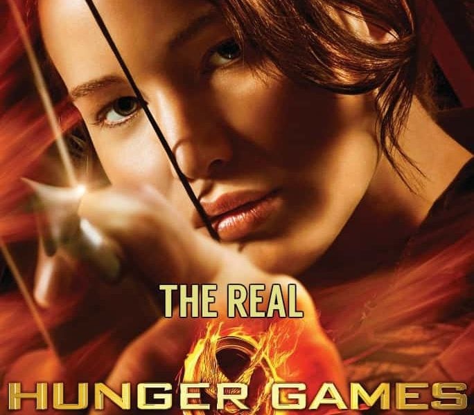 Jennifer Laurence on the poster for the first Hunger Games Film. He holds a bow and arrow in one hand. The words The Real have been added to the poster above the words Hunger Games