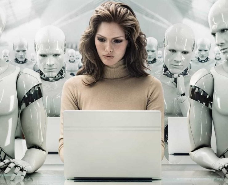 A women working on a laptop sits in a room full of human looking robots made out of shiny plastic