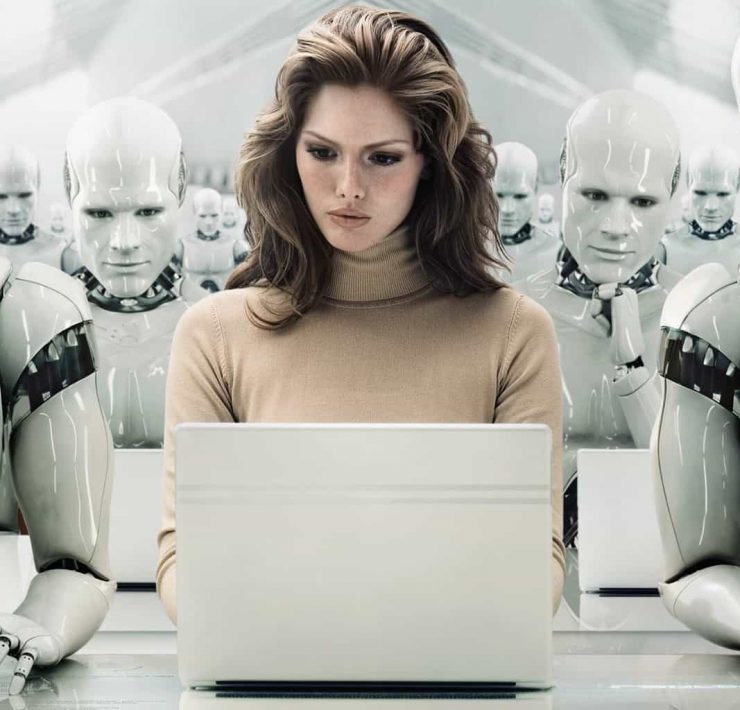 A women working on a laptop sits in a room full of human looking robots made out of shiny plastic