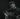 Folk musician John Smith stood playing his guitar with his eyes closed. The photograph is black and white and he is wering a dark shirt with white buttons