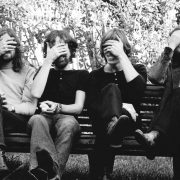 The band Pink Flord sit on a bench in a 70s black and white picture with their hands over their eyes