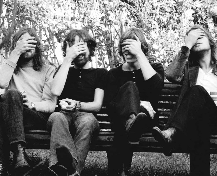 The band Pink Flord sit on a bench in a 70s black and white picture with their hands over their eyes