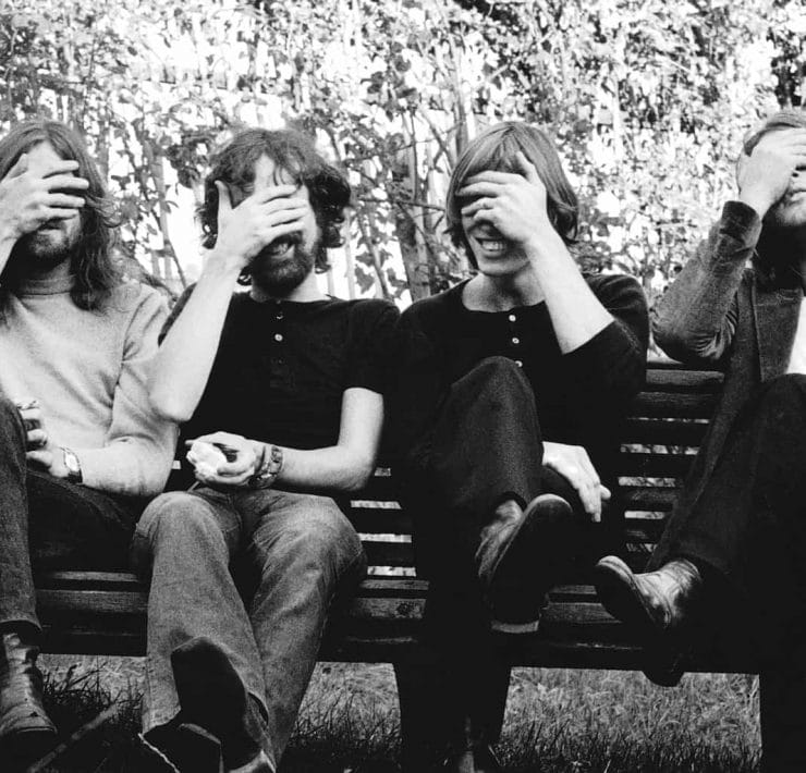 The band Pink Flord sit on a bench in a 70s black and white picture with their hands over their eyes