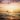 A surfer lies on his board ready to catch a wave as the sun sets below the horizon of the sea behind him