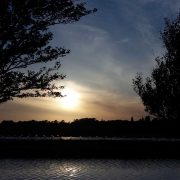 Sunset behind two trees on either side. A canal is seen in the foreground. Picture in article about living as a minimalist