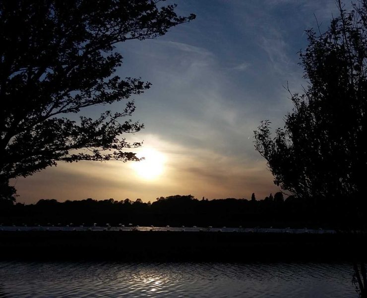 Sunset behind two trees on either side. A canal is seen in the foreground. Picture in article about living as a minimalist