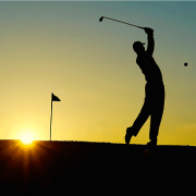 The silhouette of a golfer teeing off as the sun sets in the background