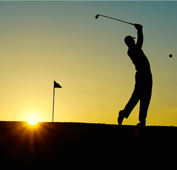 The silhouette of a golfer teeing off as the sun sets in the background