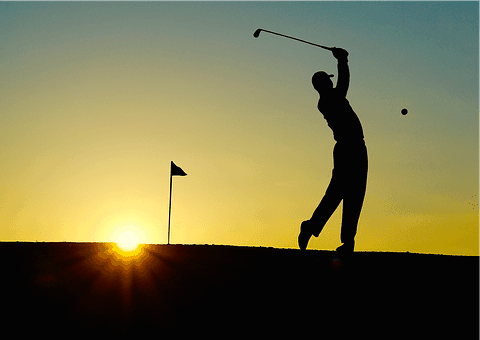 The silhouette of a golfer teeing off as the sun sets in the background