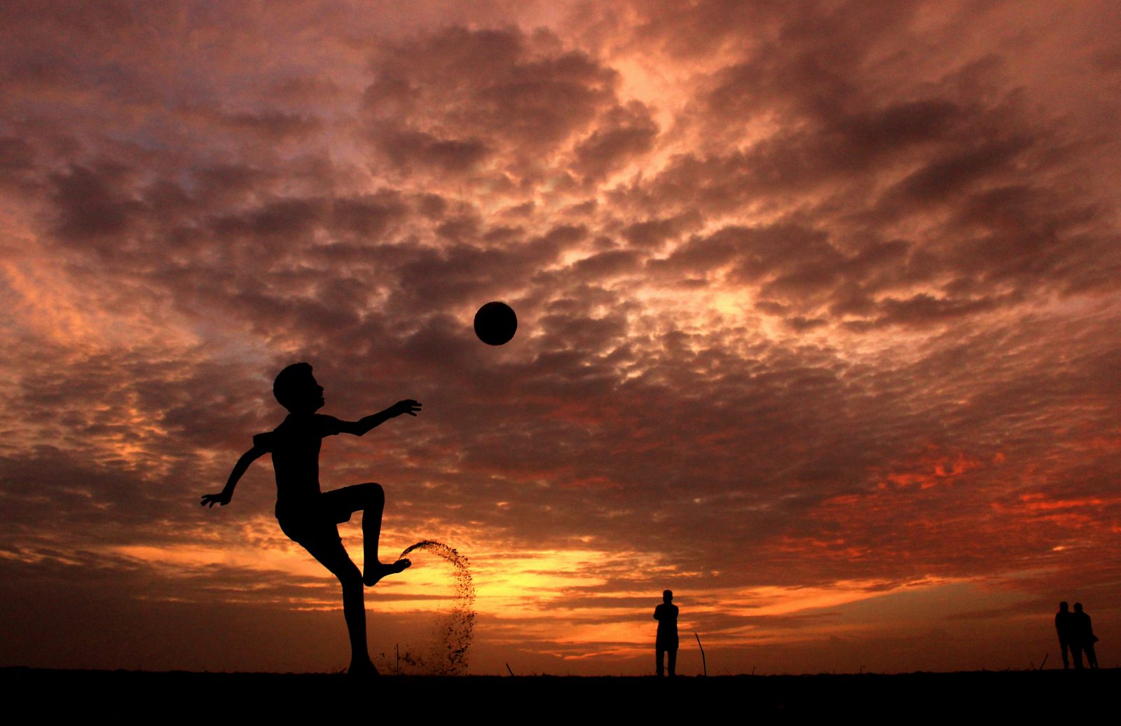 boy doing overhead kick on the beach with a sunset behind