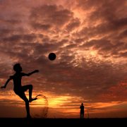 boy doing overhead kick on the beach with a sunset behind