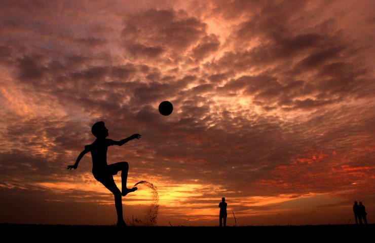 boy doing overhead kick on the beach with a sunset behind