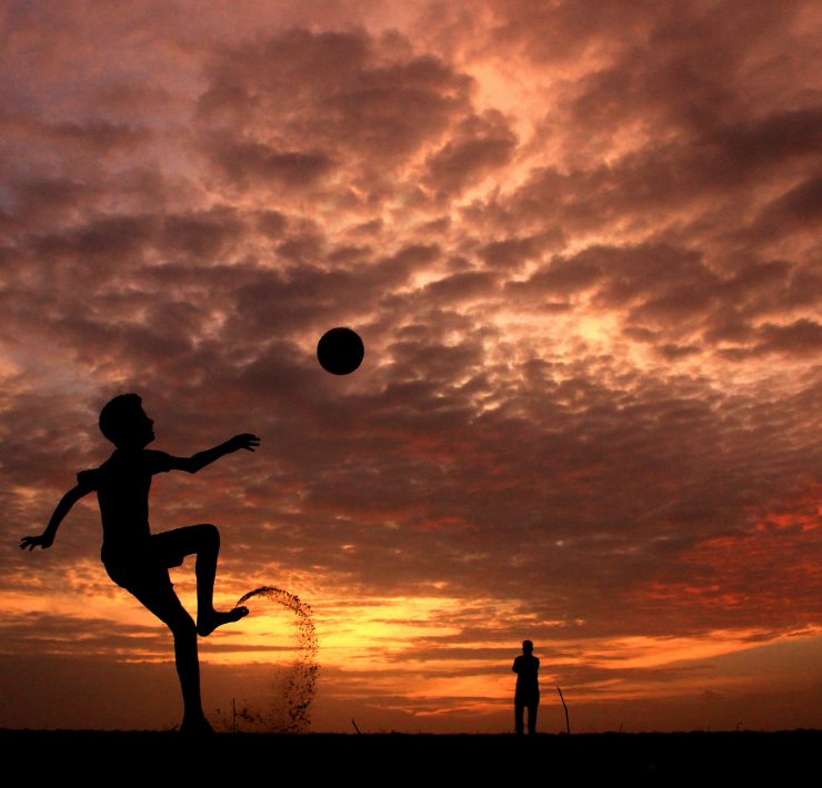 boy doing overhead kick on the beach with a sunset behind