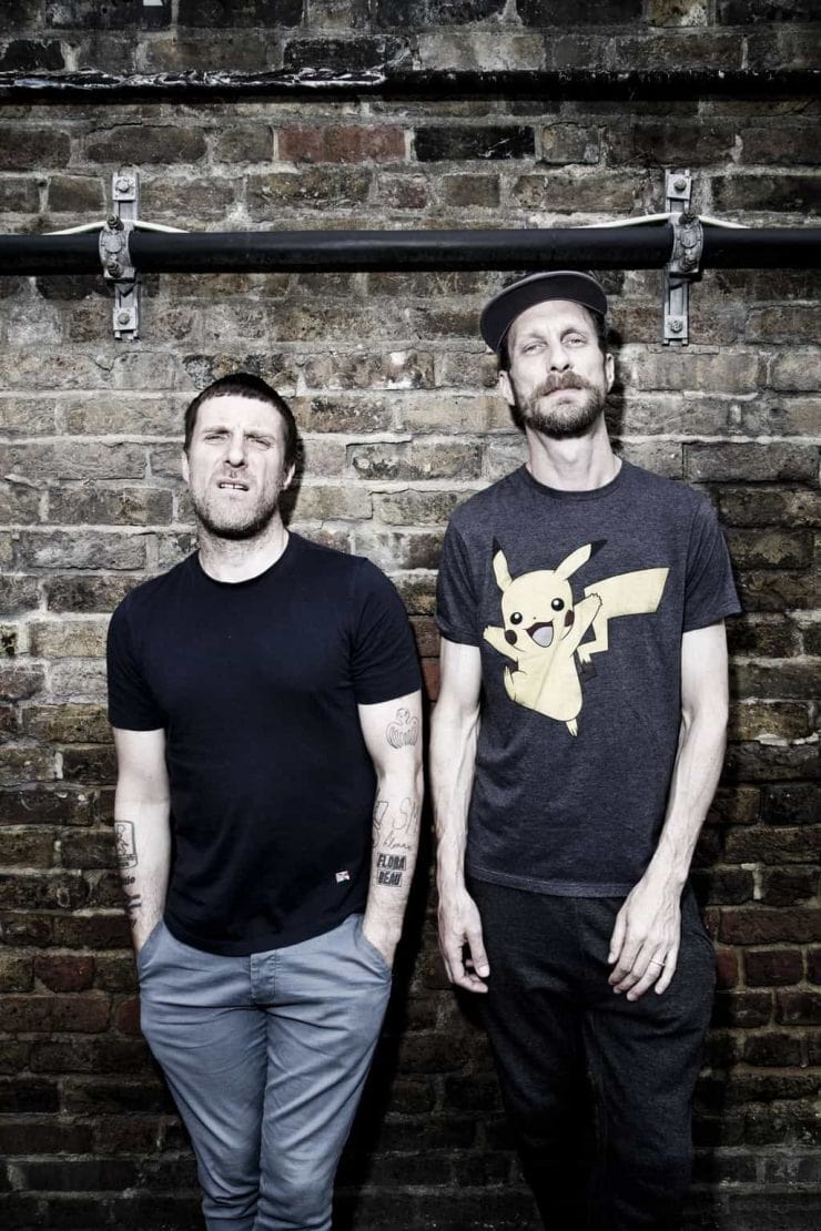Sleaford Mods stood against a wall