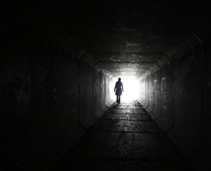 The silhouette of a man in a dark tunnel walking towards the light