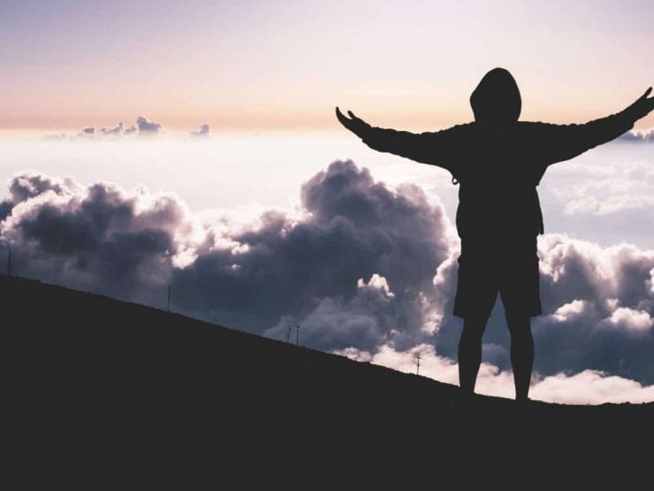 A man at the top of a mountain looking at the clouds