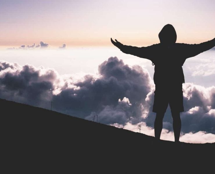 A man at the top of a mountain looking at the clouds