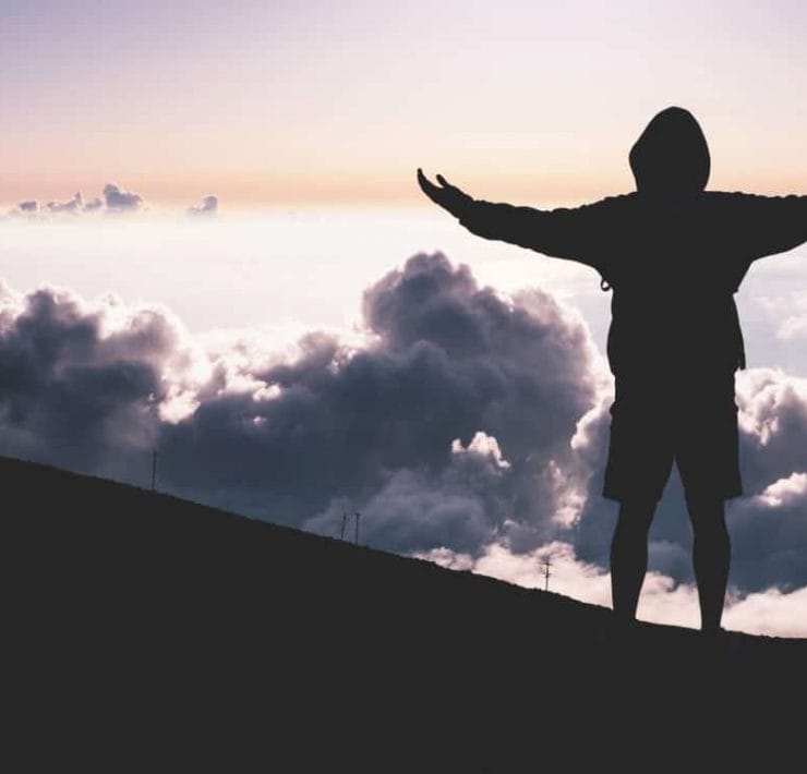 A man at the top of a mountain looking at the clouds