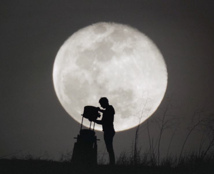 A man sets up a telescope in front of the moon