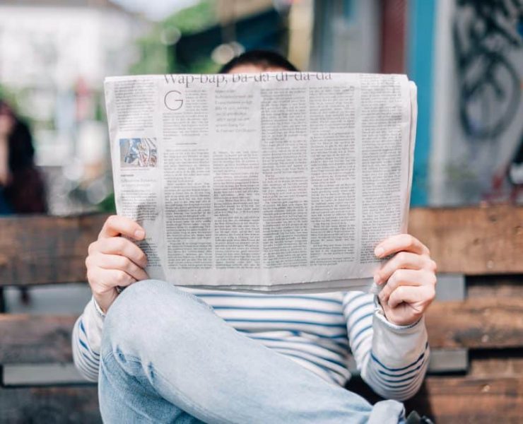 A man seated on a bench reading a newspaper