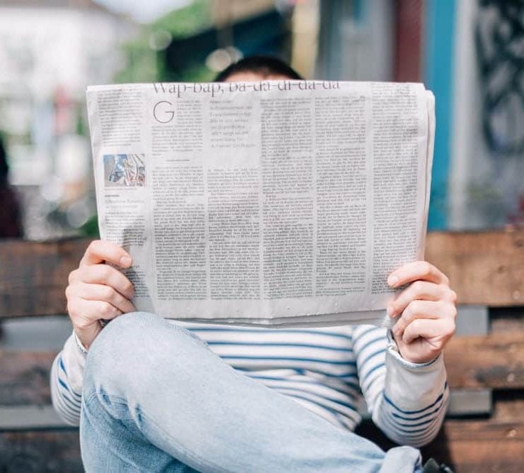A man seated on a bench reading a newspaper