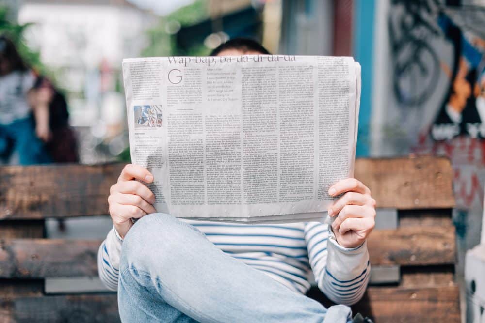 A man seated on a bench reading a newspaper