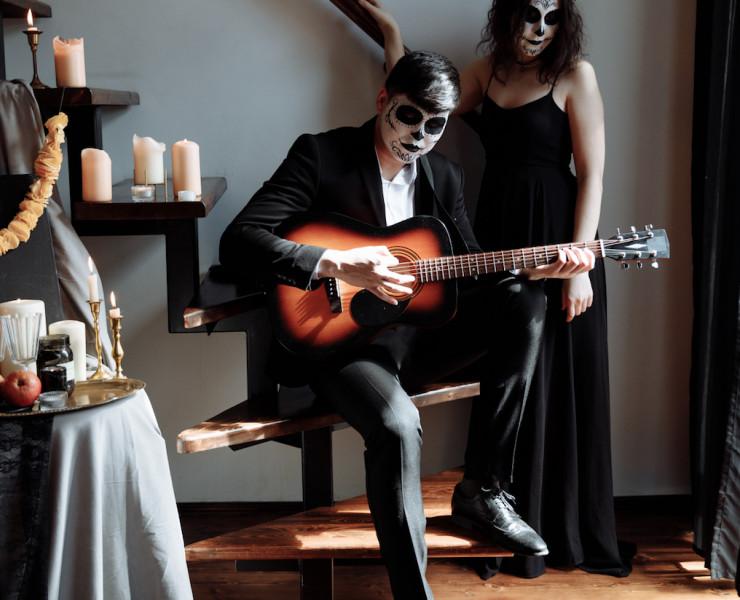man with face painted in spooky way playing guitar in front of woman