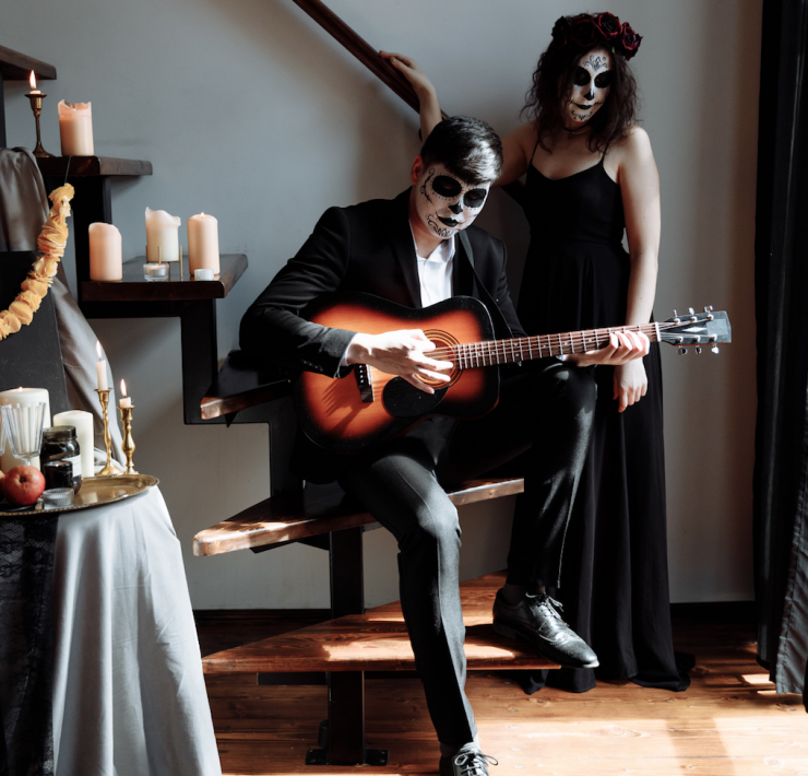 man with face painted in spooky way playing guitar in front of woman