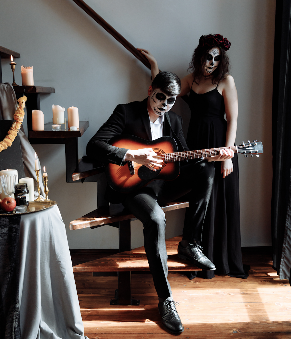 man with face painted in spooky way playing guitar in front of woman