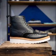 A black leather brogue boot on a wooden stand