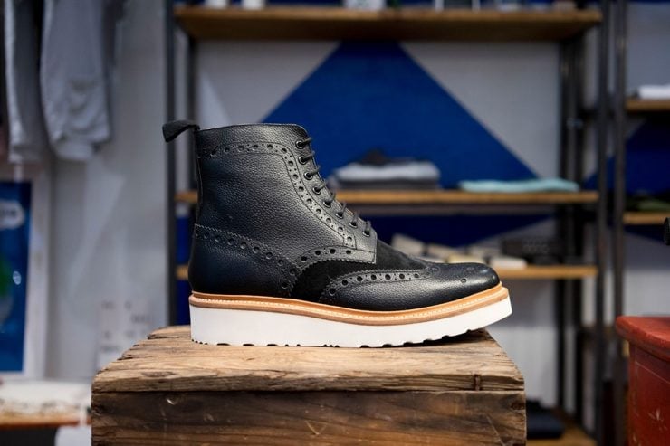 A black leather brogue boot on a wooden stand