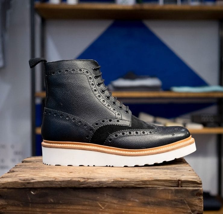 A black leather brogue boot on a wooden stand