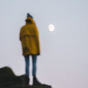 Man stood on rock in yellow jacket looking at the moon