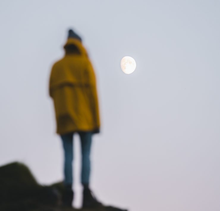 Man stood on rock in yellow jacket looking at the moon