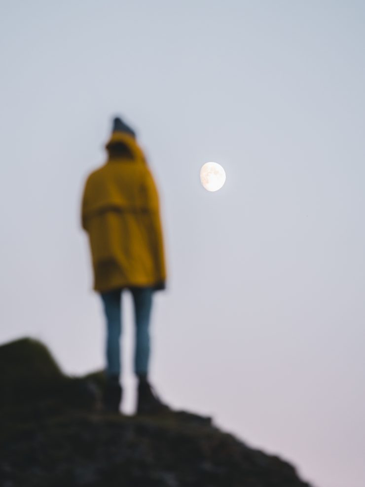 Man stood on rock in yellow jacket looking at the moon