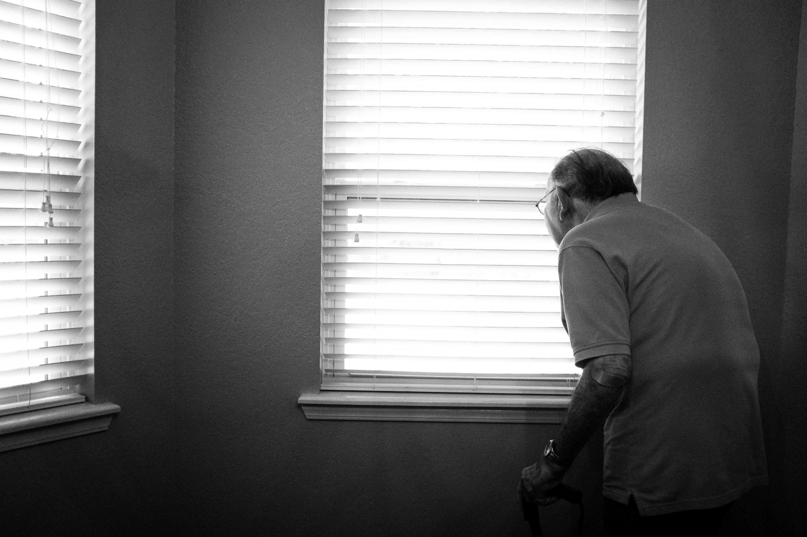 Old man peering through blinds in his house