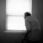 Old man peering through blinds in his house