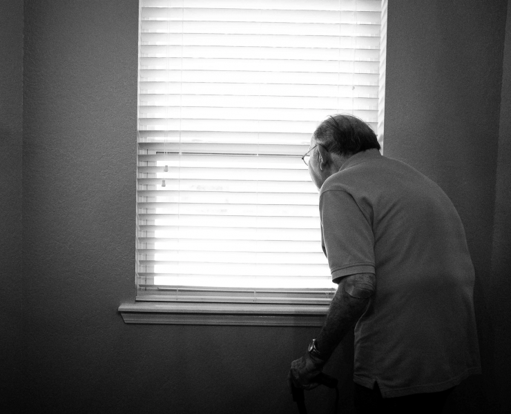 Old man peering through blinds in his house