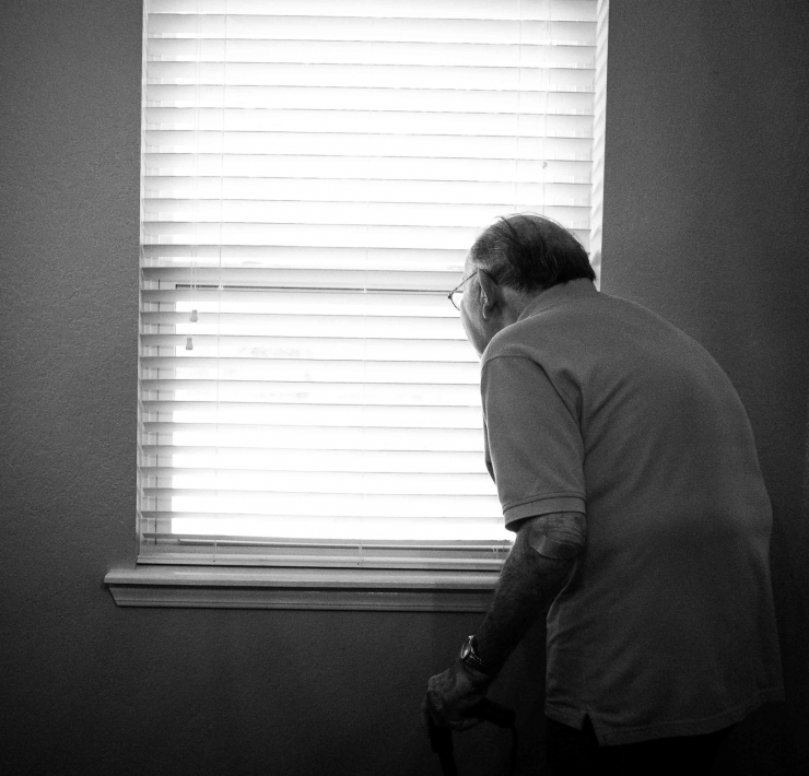 Old man peering through blinds in his house