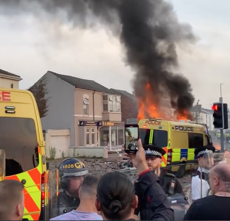 a crowd watch a riot van on fair in Southport