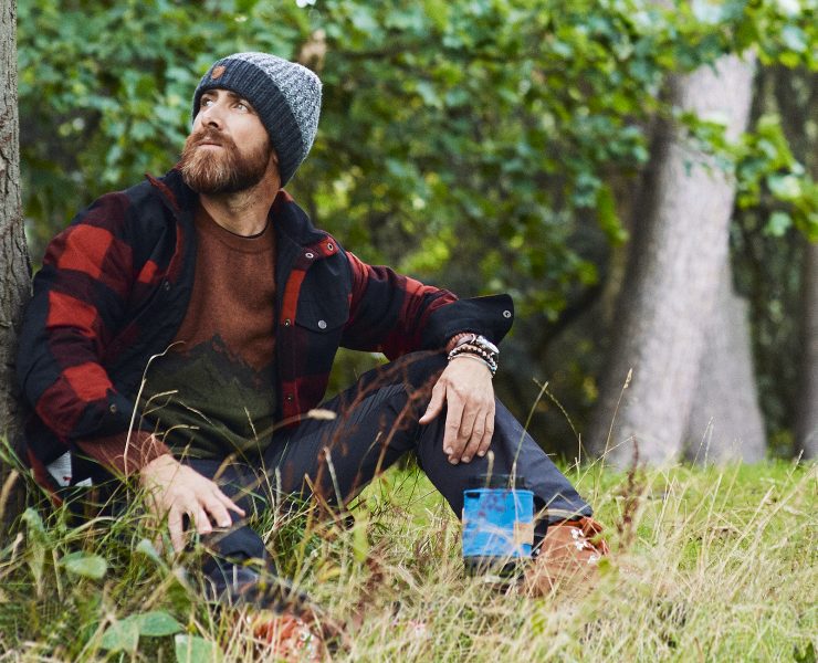 Aldio Kane sat by a tree wearing the Fjӓllrӓven Clothing Range