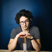 Alexis Ainouz sitting at a table with a chef's knife
